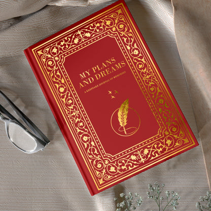 Red book titled 'My Plans and Dreams' on a textured surface with a plant and scissors.