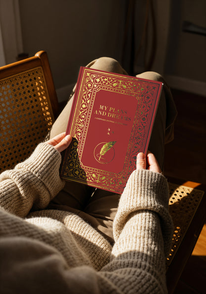 Person holding a red book titled 'My plans and dreams' in a cozy setting.